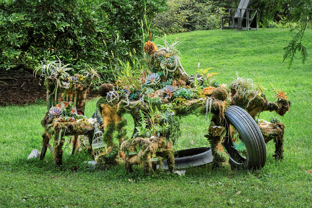 An outdoor installation of Found Furniture, Wire, Coconut Matte, Pillow Moss, Live Succulents, Air Plants, Grass, Found Tires, and Found Natural Materials