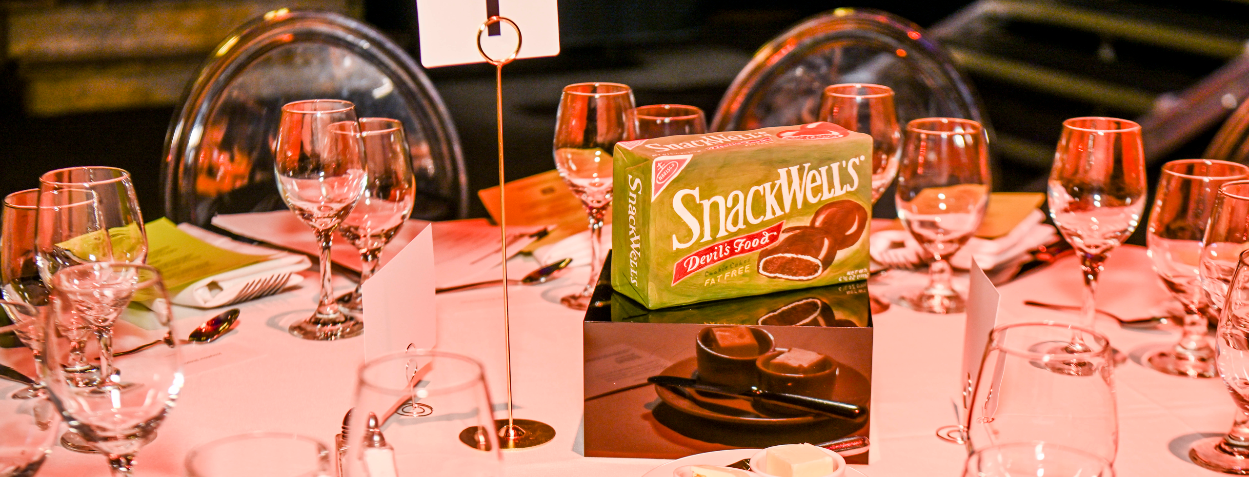 A work by Stephanie H. Shih on a pedestal as a centerpiece on one of the dinner tables. It is a ceramic piece that replicates a SnackWell's devil's food cake box.