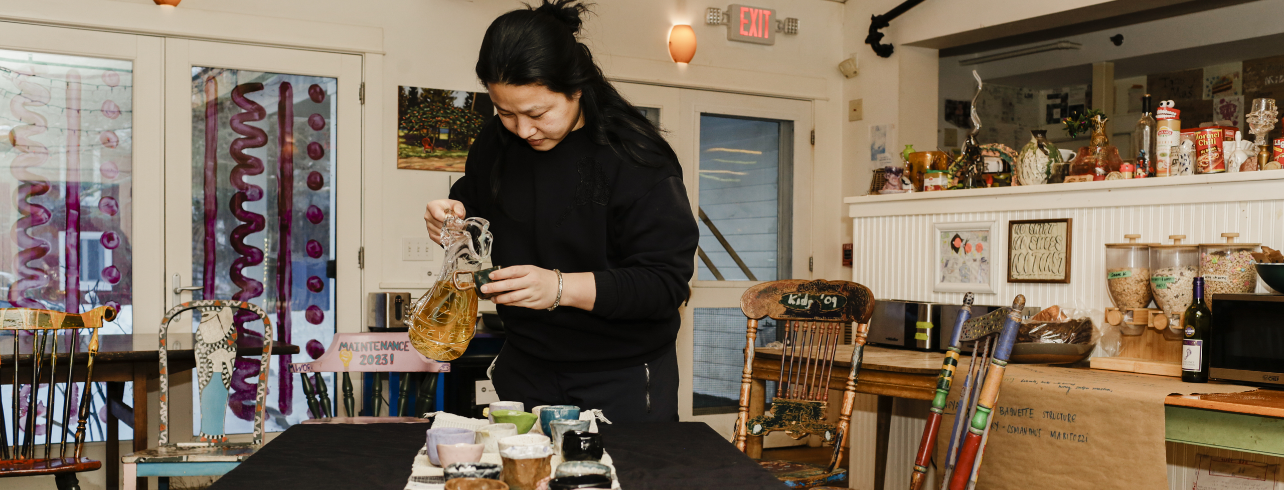An individual pours tea into a handmade teacup in a creative dining room setting.