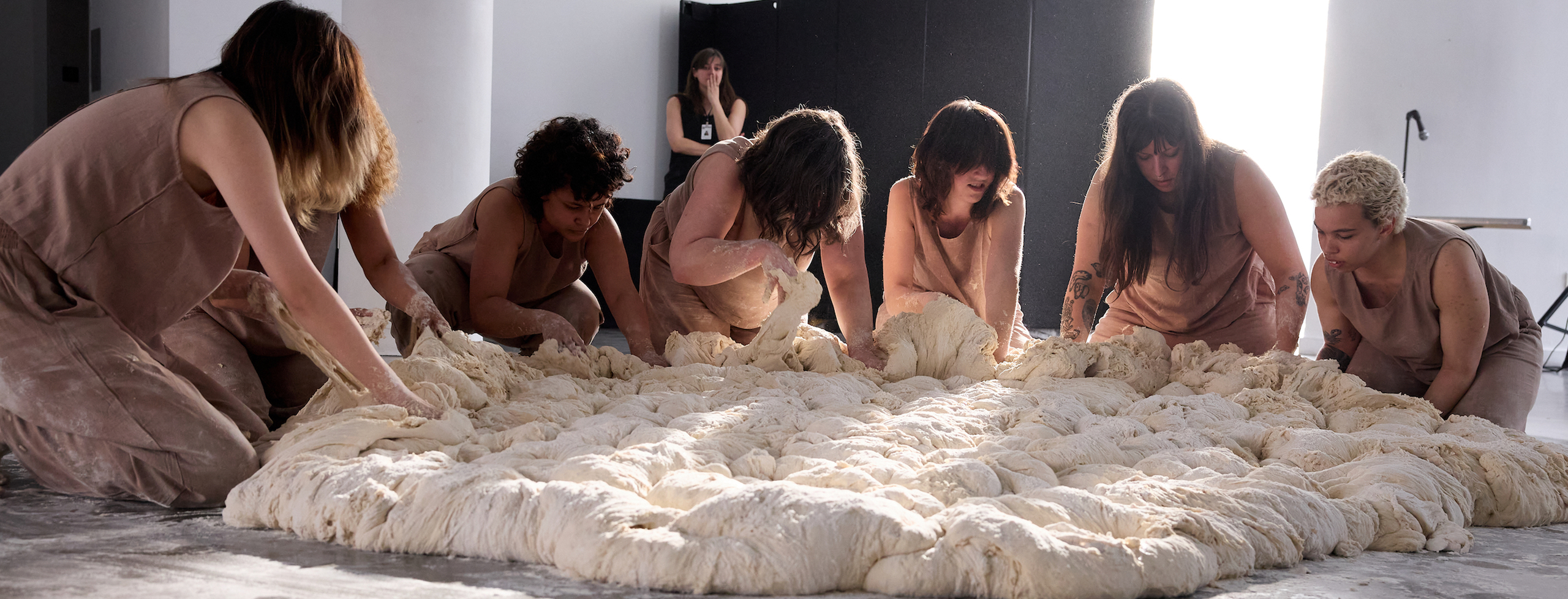 Seven women bend over on the floor creating their collecting weight in bread dough for a performance that happened at the Bronx Museum in 2023.